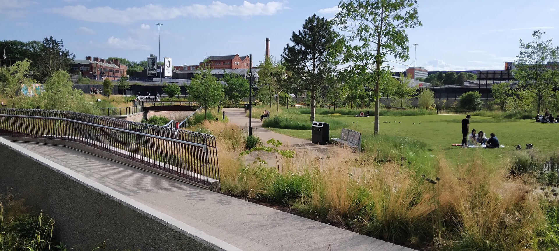 Mayfield Park, Manchester: planted banks, a footbridge and open lawn beneath former railway buildings